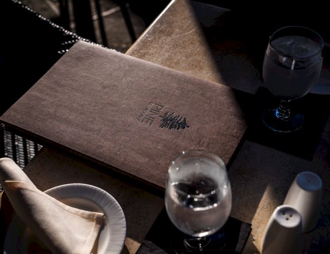 A dining table set with a menu, water glasses, napkins, and salt and pepper shakers, illuminated by sunlight.