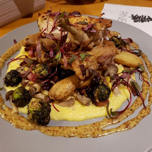 The image shows a plate of food featuring sliced roasted meat on top of creamy polenta, with Brussels sprouts and fingerling potatoes, garnished with herbs.