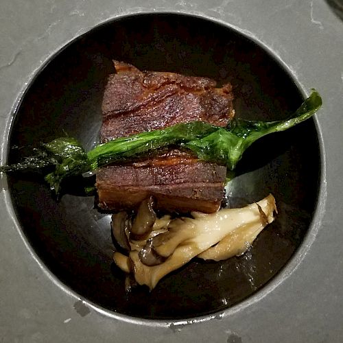 A plate with a piece of meat, a green vegetable, and mushrooms arranged elegantly on it.