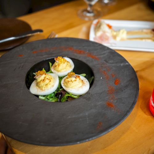 A plate of deviled eggs is in the foreground, with a refreshing red drink and other dishes in the background on a wooden table.