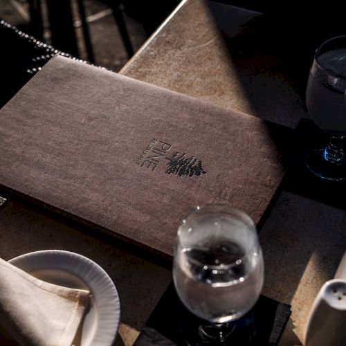 A restaurant table set with water glasses, folded napkins, and a wooden menu featuring an embossed logo and text in an Asian script.