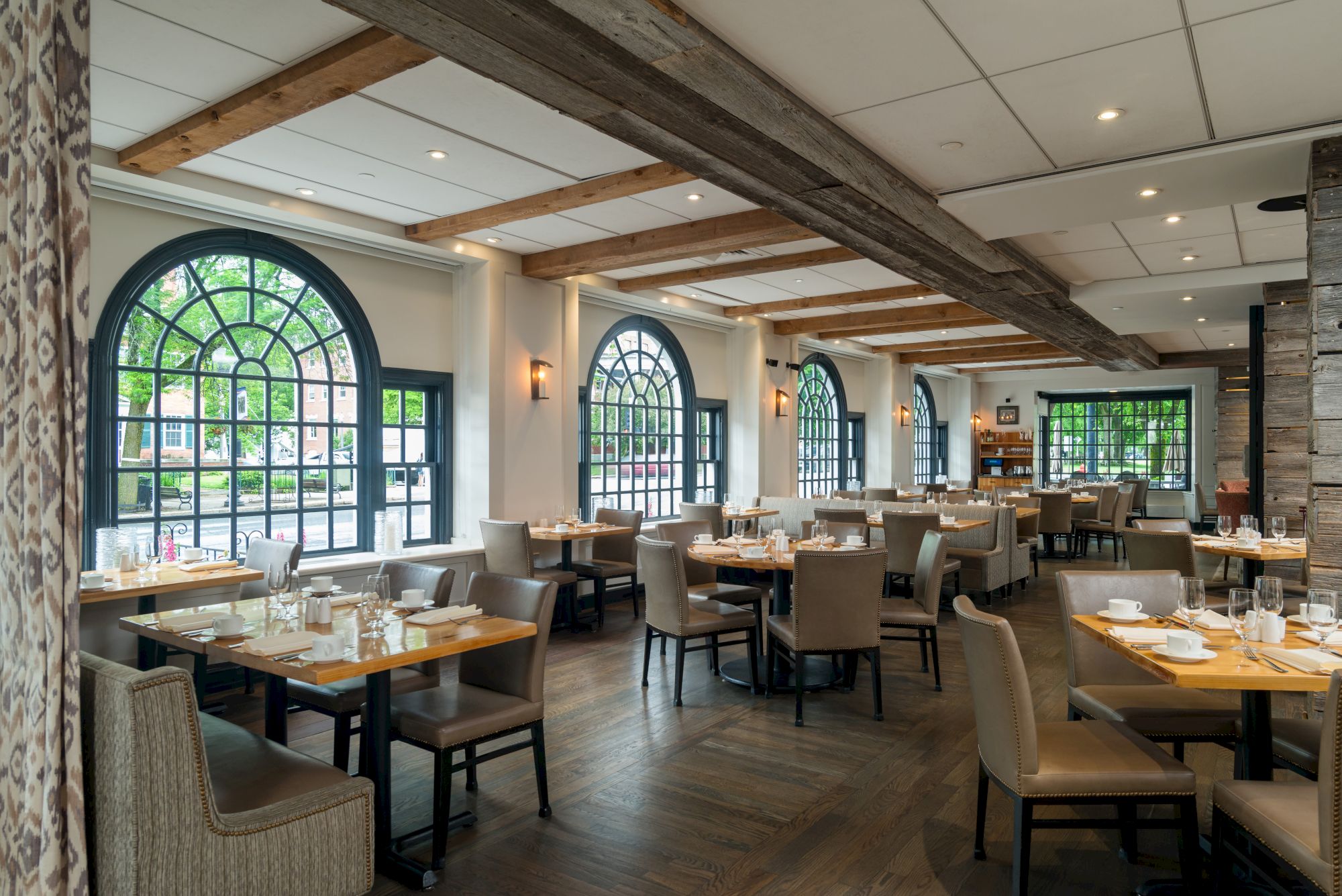 This image shows a spacious and elegant restaurant with large arched windows, wooden beams, and neatly set tables and chairs in a modern setting.