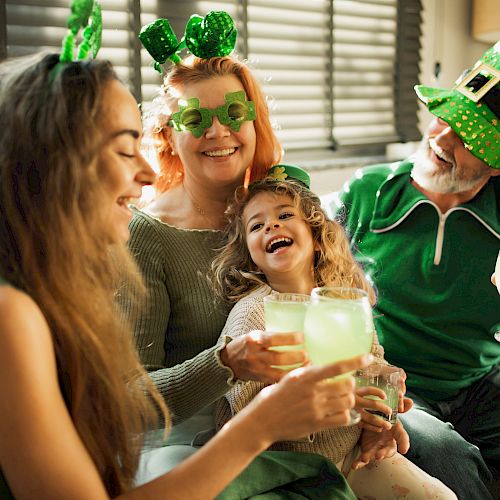 A joyful group celebrates with drinks, wearing green clothes and hats, possibly for St. Patrick's Day, smiling and enjoying together.