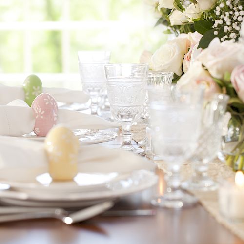 A beautifully set table with floral arrangements, glassware, and decorated eggs on plates, ready for a special occasion or celebration.